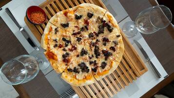 A pizza on a wooden board with a fork and knife beside it.