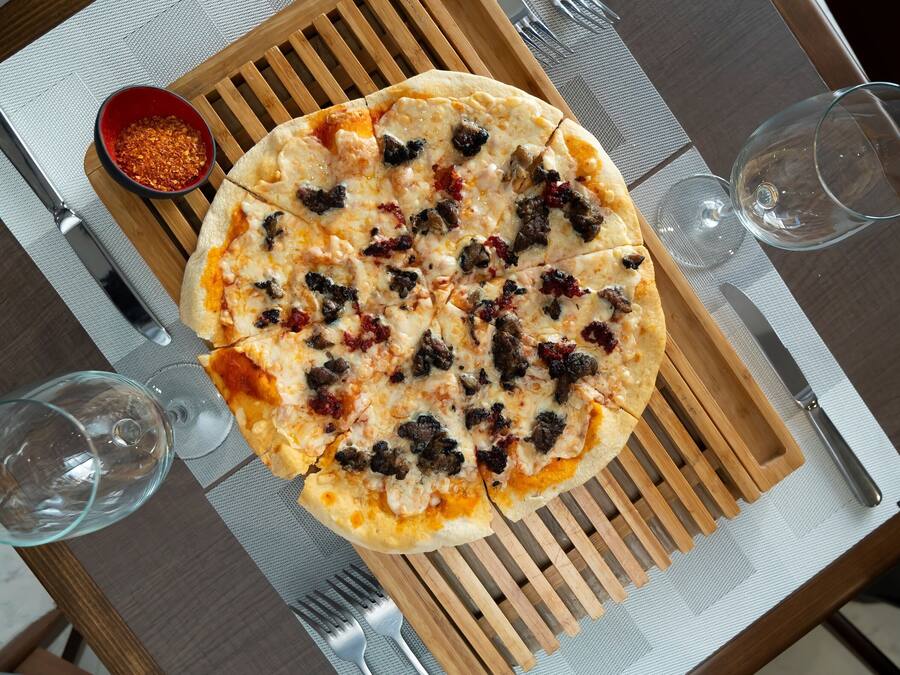 Una pizza sobre una tabla de madera, con un tenedor y un cuchillo a un lado.