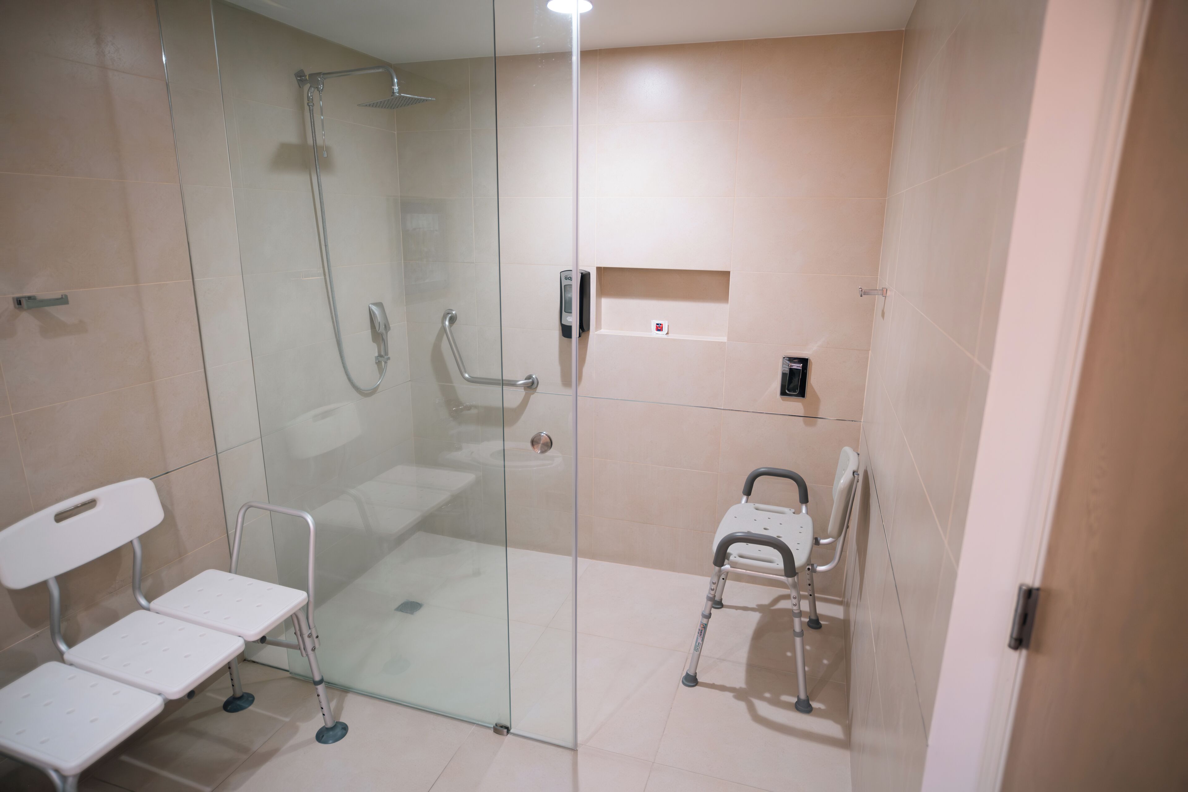 Un baño con cabina de ducha de vidrio, un banco blanco y una silla de ruedas.
