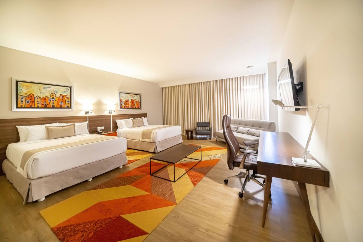 Habitación de hotel con dos camas, un escritorio, una silla, una mesita de centro y obras de arte en las paredes.