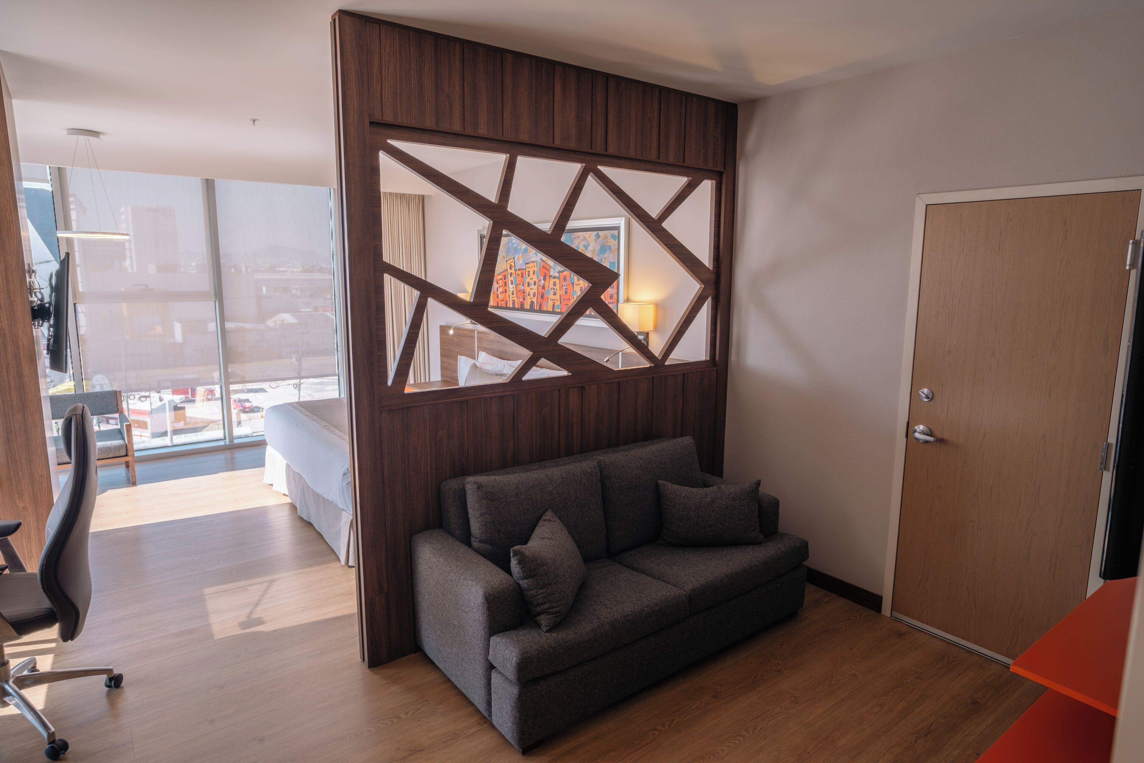 Habitación de hotel moderna con sofá, escritorio y vistas a la ciudad.