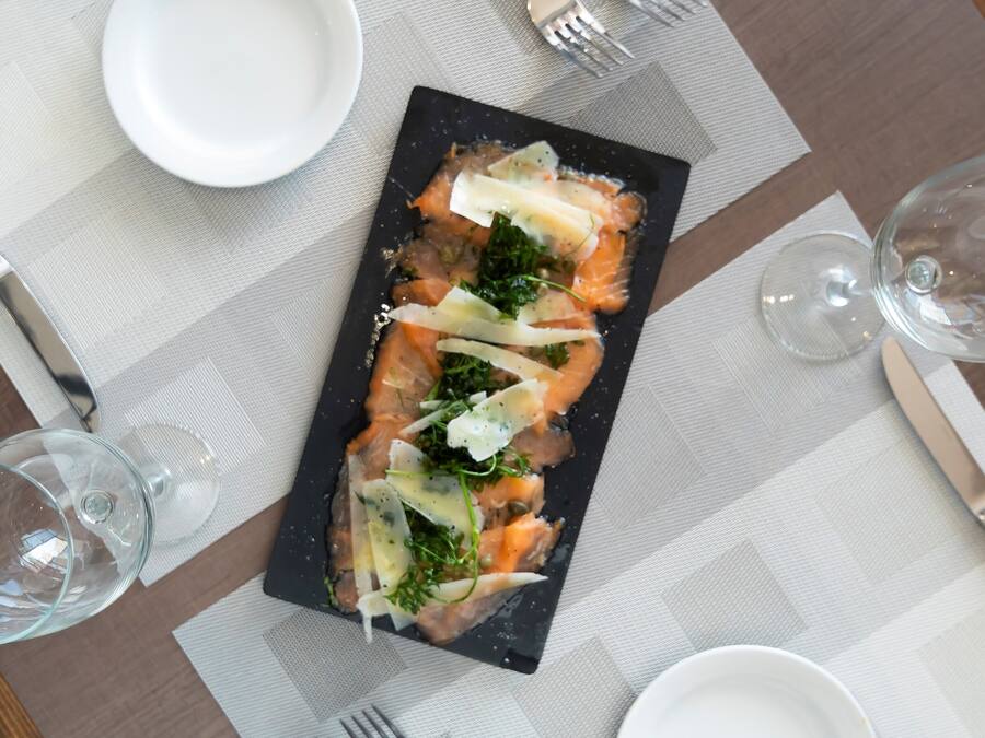 Una mesa de comedor ordenada con un plato rectangular negro de comida, una copa de vino y cubiertos.