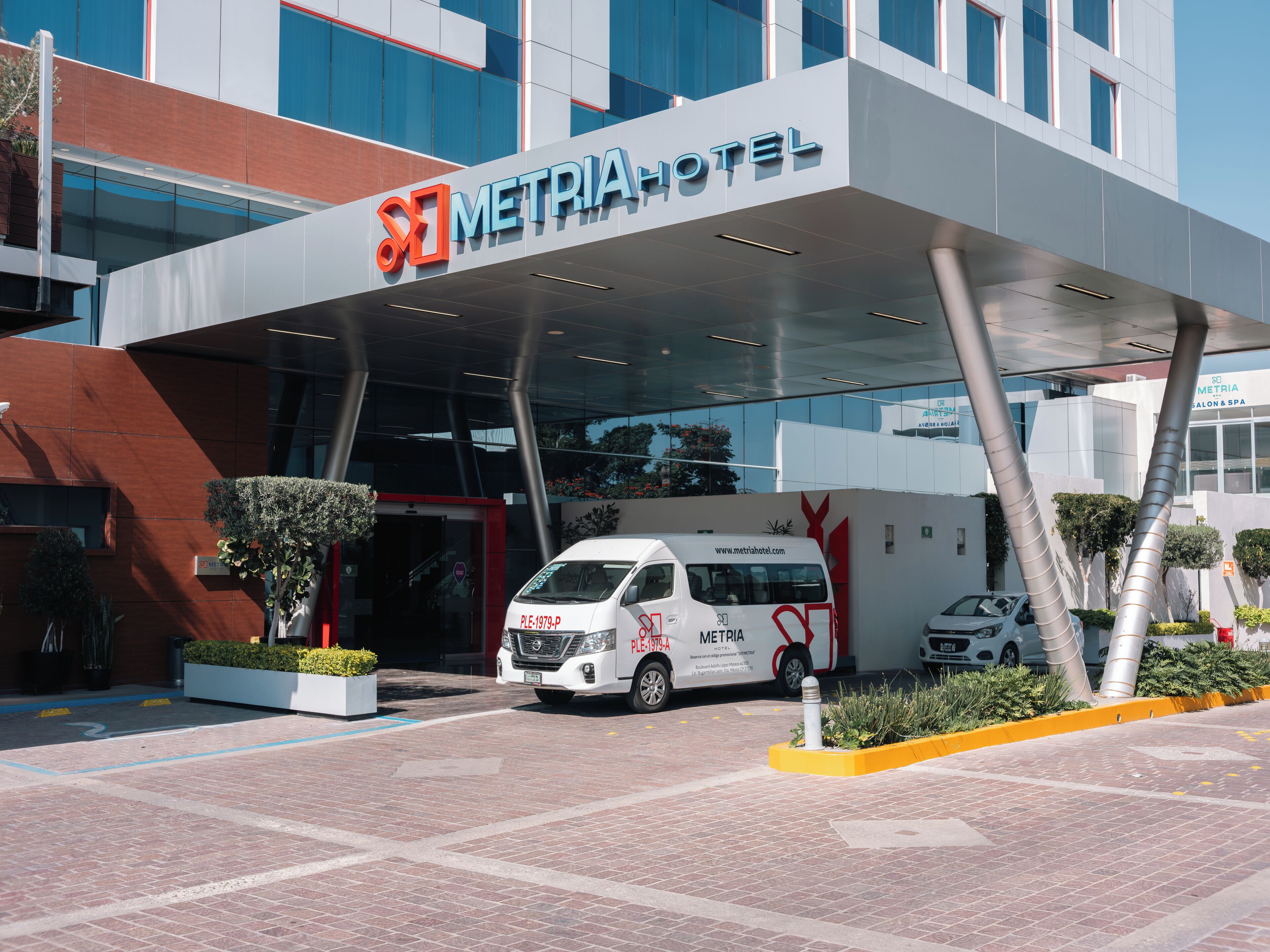 A modern hotel entrance with a prominent sign, a white van, and a well-maintained outdoor area.
