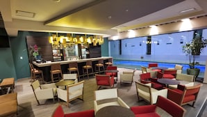 A modern indoor bar area with seating arrangements, a pool view, and a bar counter. - Metria Hotel  (León)
