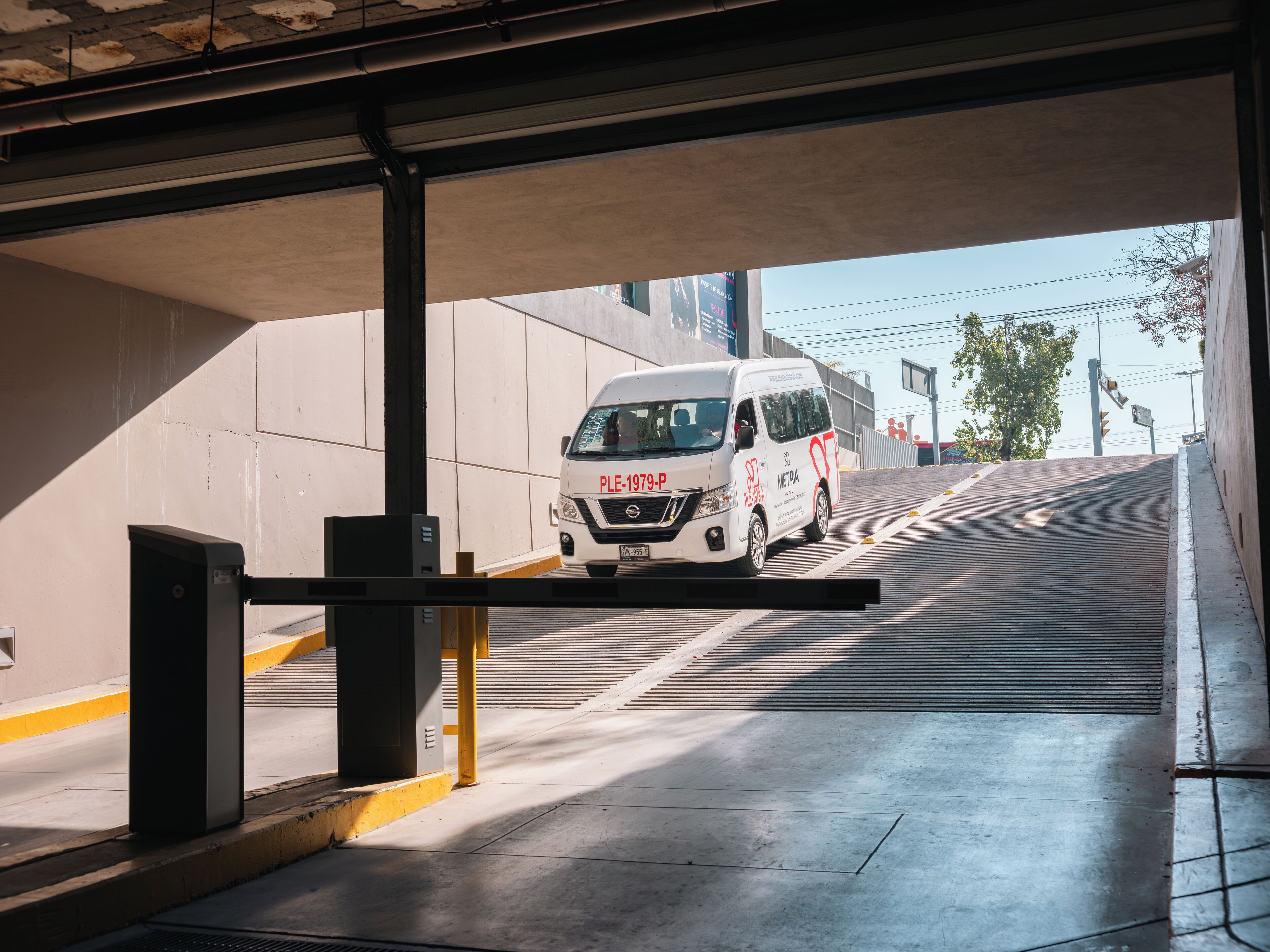 A white van with red text and a website address on its side, parked under a covered area with a metal barrier.