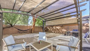 Eine Terrasse im Freien mit überdachter Sitzgruppe, einer Hängematte und einem Grill.