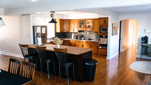A modern kitchen with wooden cabinets, a central island with bar stools, a stainless steel refrigerator, and a microwave. - Grings Hill Guest House (Sinking Spring)