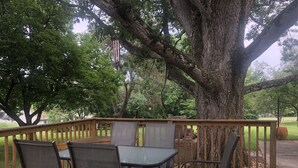 A wooden deck with a table and four chairs, surrounded by large trees. - Grings Hill Guest House (Sinking Spring)