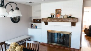 A living room with a fireplace, a dining table with chairs, a bench, and a bookshelf. - Grings Hill Guest House (Sinking Spring)