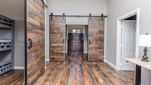 Una habitación con piso de madera, una puerta corredera estilo granero, una puerta blanca y una mesa con lámpara.