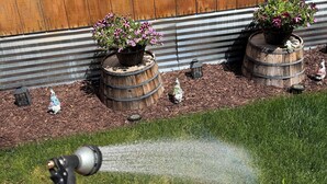 Een tuin met bloempotten, een houten vat en een decoratieve lantaarn.