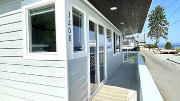 A white building with the number 3208, a covered porch, and a view of the street and ocean.