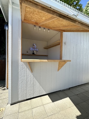 Eine kleine Außenbar mit einer Neonreklame, Holzregalen und einem geneigten Dach.