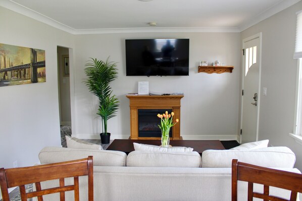 A living room with a sofa, a flat-screen TV, a fireplace, and a potted plant. - Walk to Queen St • Shaw Festival • Local Shops • Wineries (Niagara-on-the-Lake)