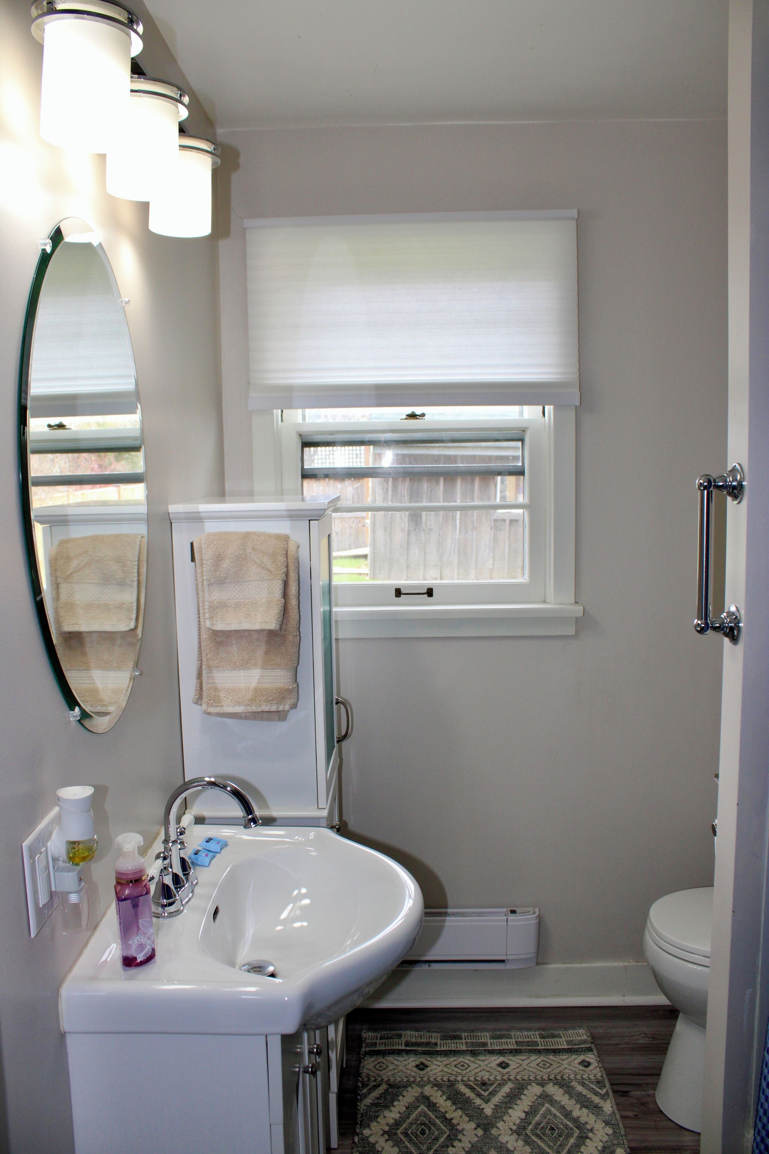 A bathroom with a sink, mirror, towel rack, window, and toilet.