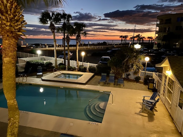 A swimming pool with lounge chairs and a view of the sunset over the ocean.