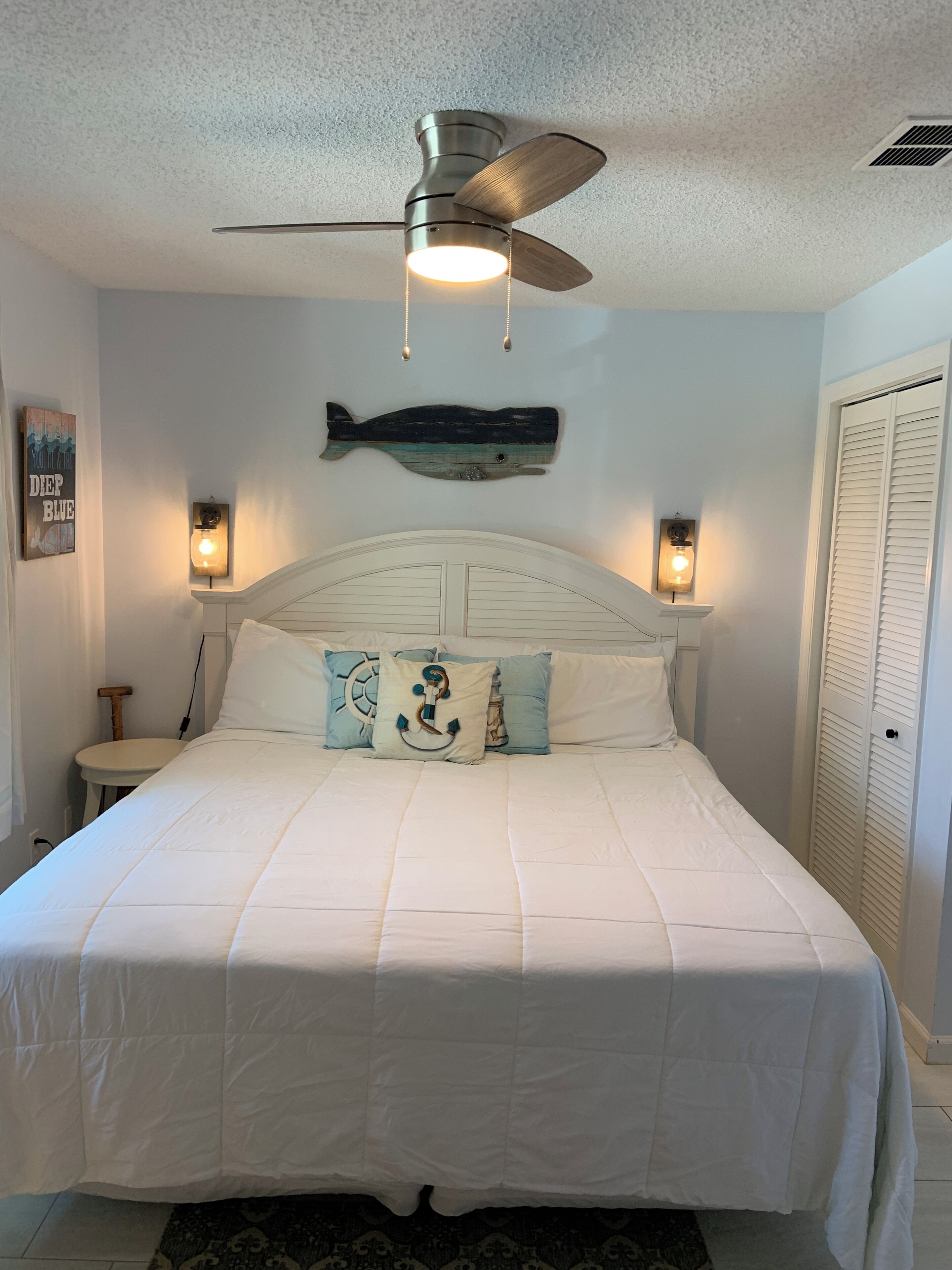 A bedroom with a bed, a ceiling fan, wall-mounted lights, a fish decoration, and a door with louvered shutters.