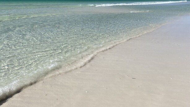 Une plage avec une eau claire et peu profonde et un rivage sablonneux.