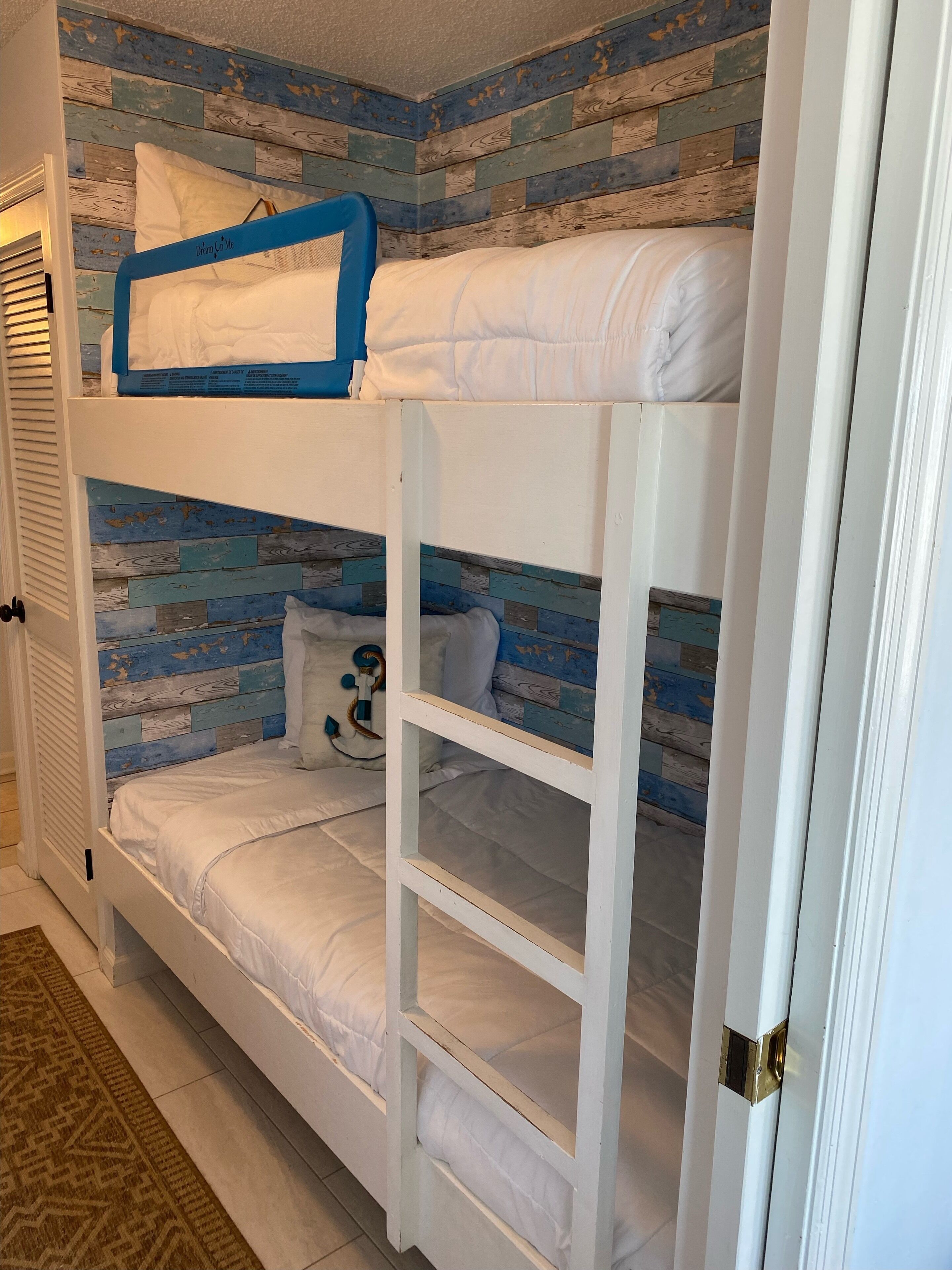 A bunk bed with a blue and white wooden headboard, white bedding, and a small decorative item on the lower bunk.