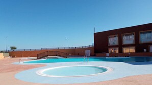 Zona de piscina con un puente, un edificio con amplios ventanales y cielo despejado.