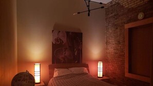 Een slaapkamer met een bakstenen muur, een bed met een beddegoed met patroon, twee bedlampjes en een wereldbol op een nachtkastje.
