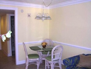 A dining area with a glass table, white wicker chairs, and a hanging light fixture.
