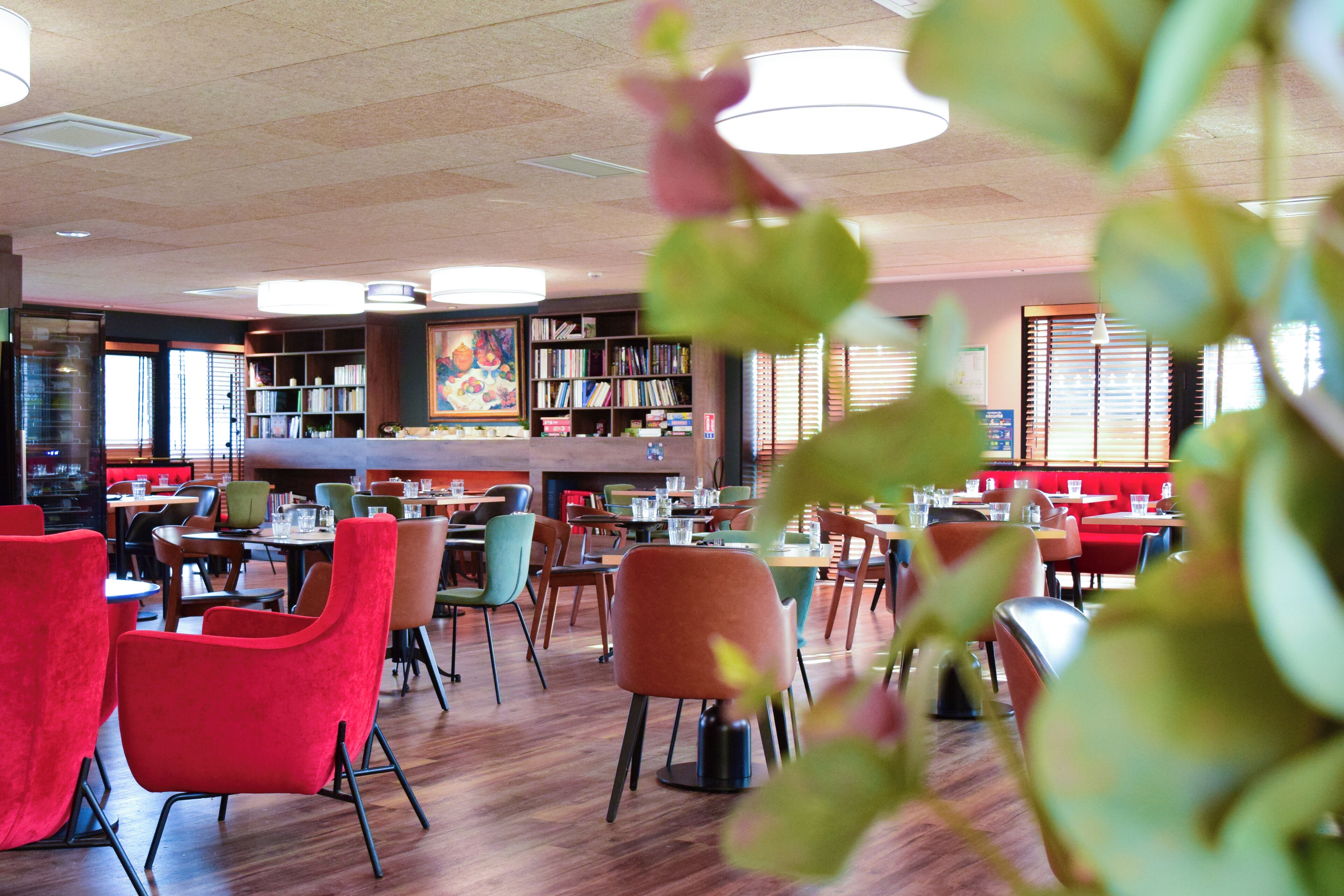 Un restaurante moderno con suelos de madera, sillas rojas y verdes, y diferentes tipos de asientos.