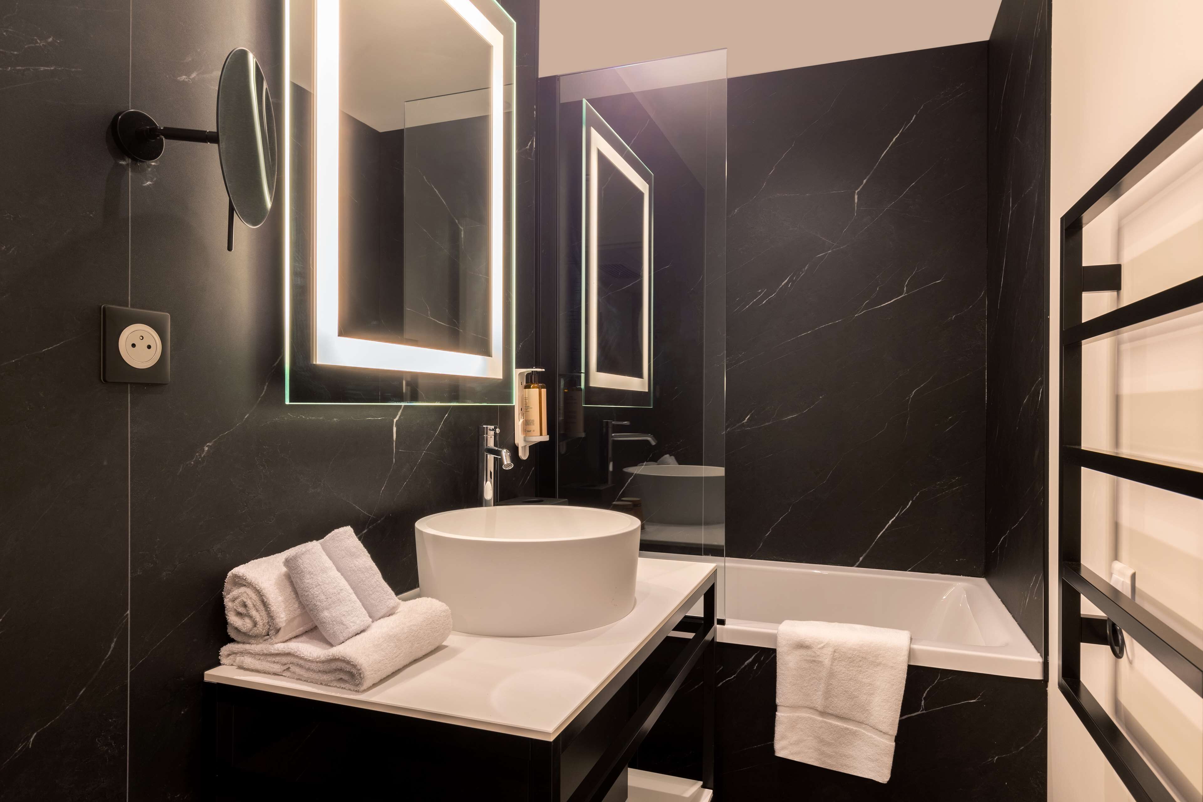 Un baño moderno con un lavabo blanco redondo, un espejo grande y una bañera negra.