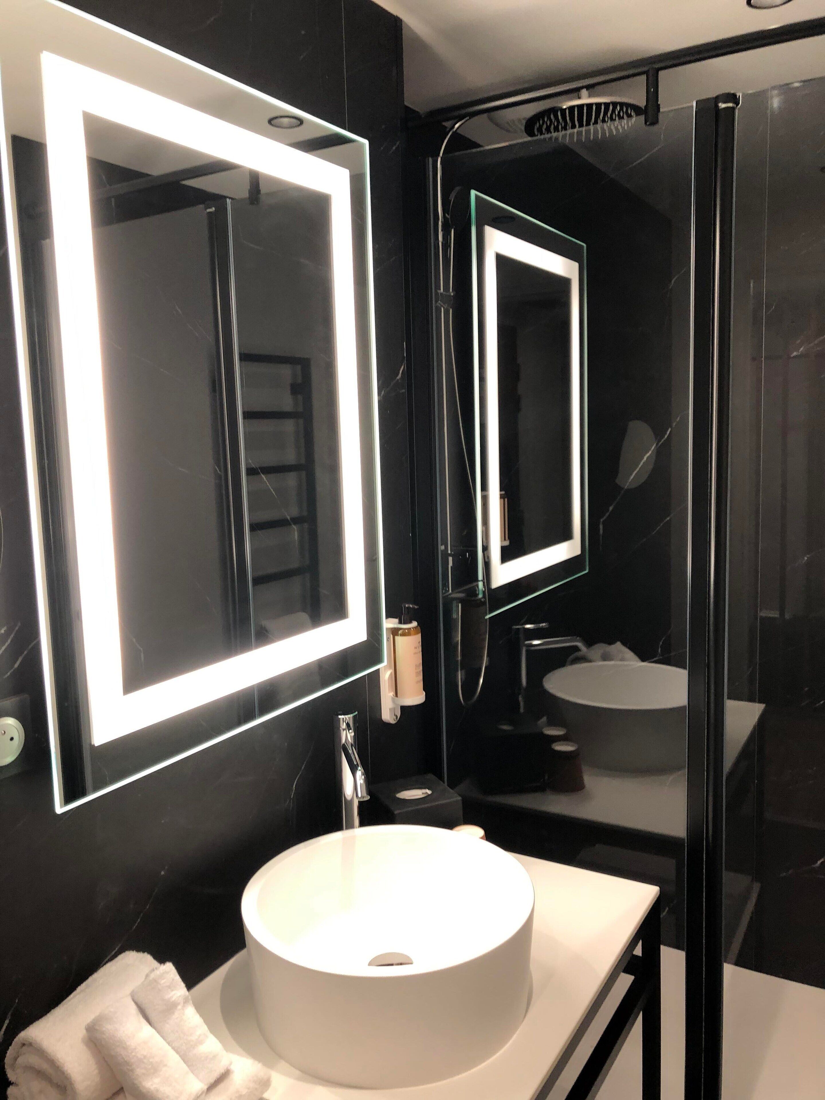 A modern bathroom with a large mirror, a round sink, and a glass shower enclosure.