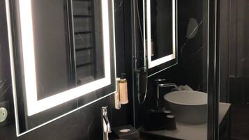 A modern bathroom with a large mirror, a round sink, and a glass shower enclosure.