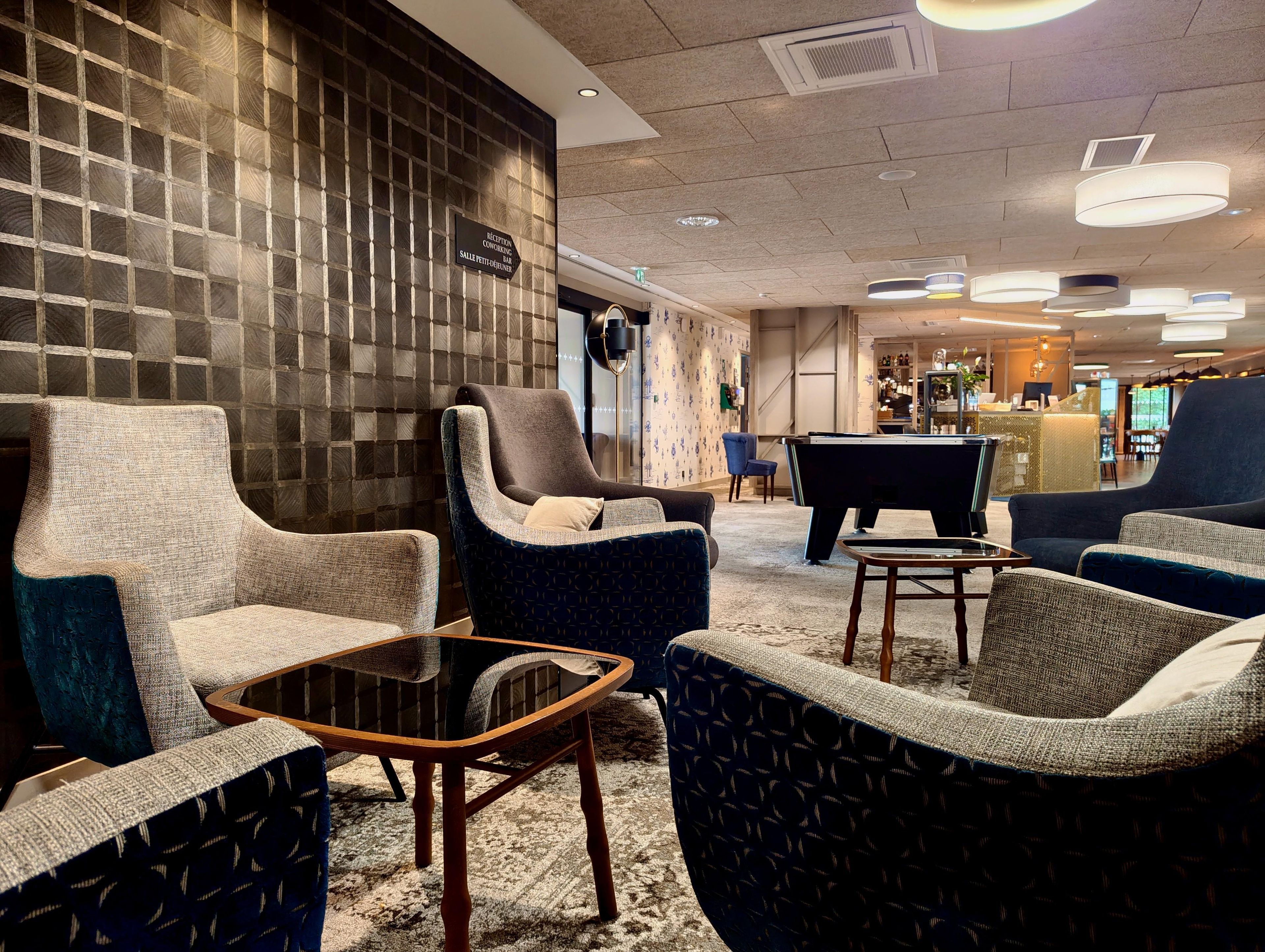 A hotel lobby with seating arrangements, a reception desk, and a pool table.