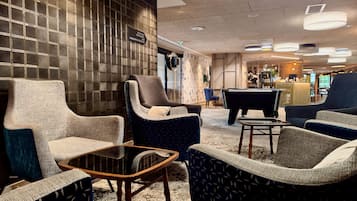 A hotel lobby with seating arrangements, a reception desk, and a pool table.