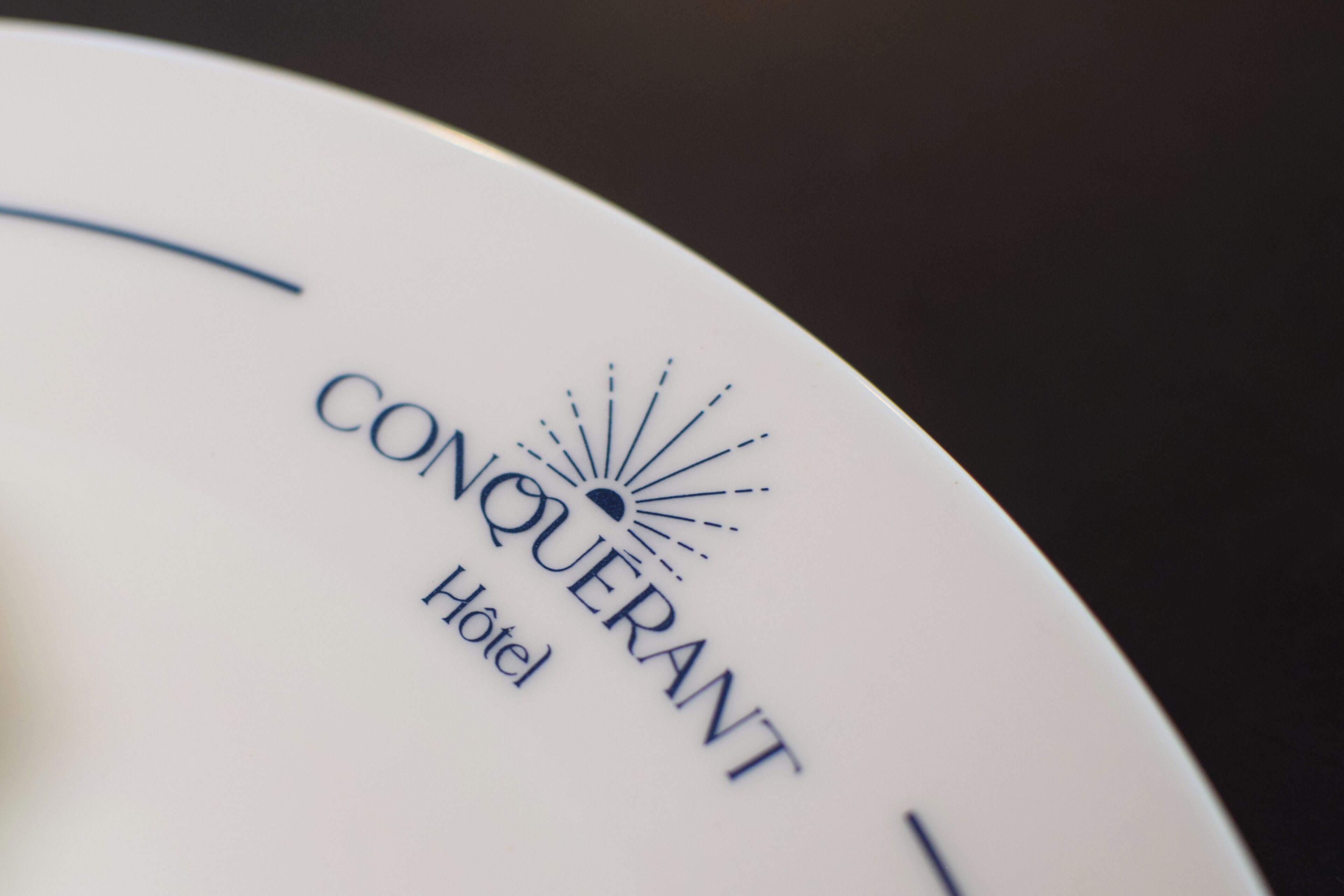 A white plate with the text "CONQUERANT Hotel" and a sunburst logo.