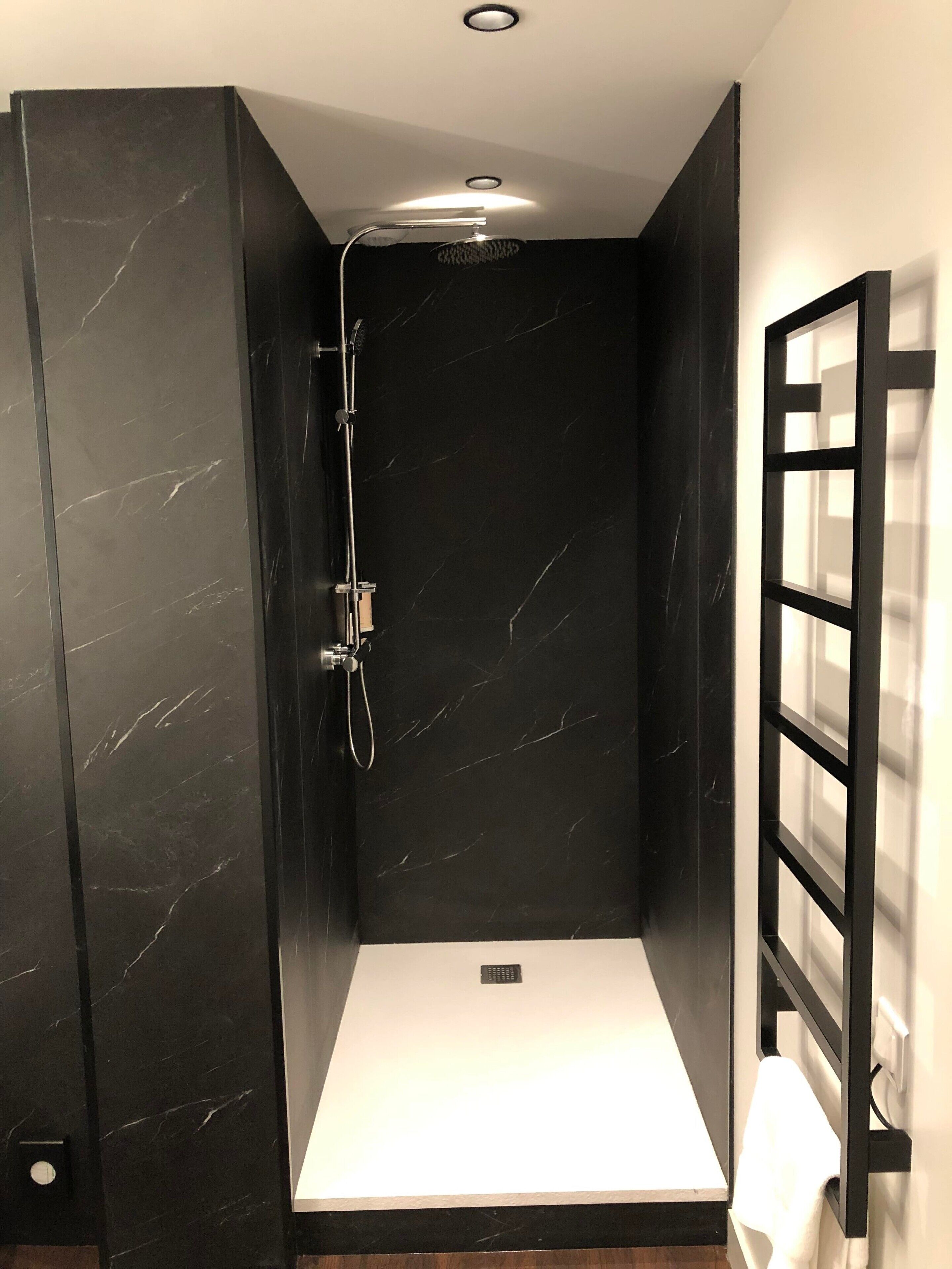 Casa de banho moderna com cabine de duche em mármore preto, lavatório branco e divisória de vidro com estrutura preta.
