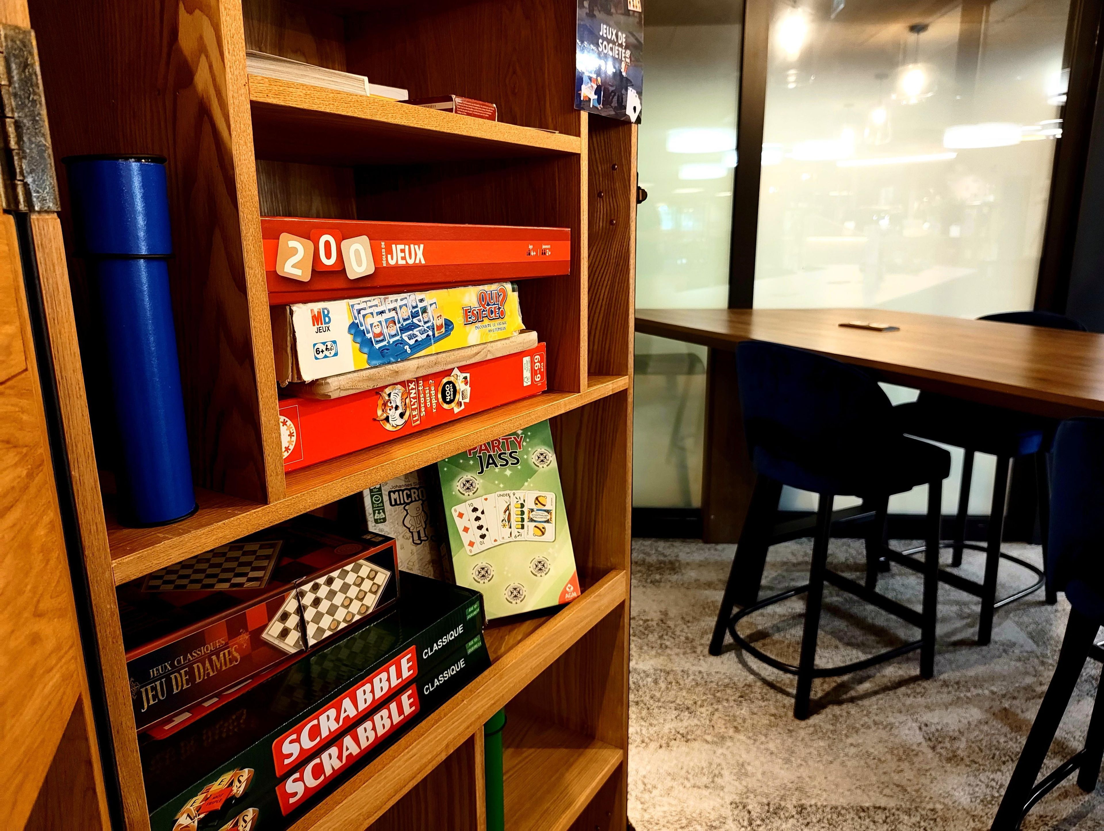 Una estantería de madera con varios juegos de mesa, un vaso azul y vistas de una habitación con una mesa y sillas.