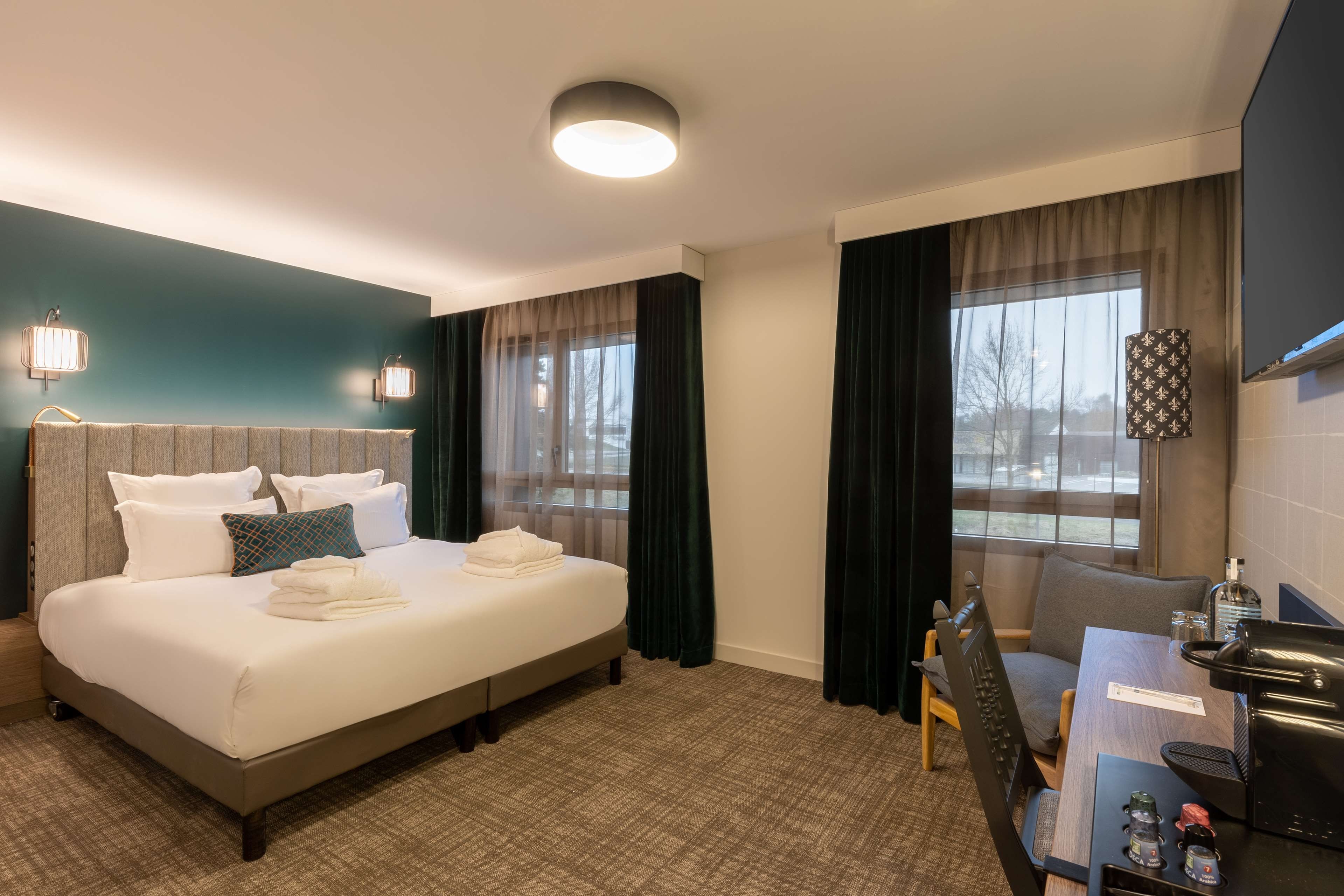Une chambre d’hôtel avec un lit, un bureau, une chaise, une table et une fenêtre avec des rideaux.