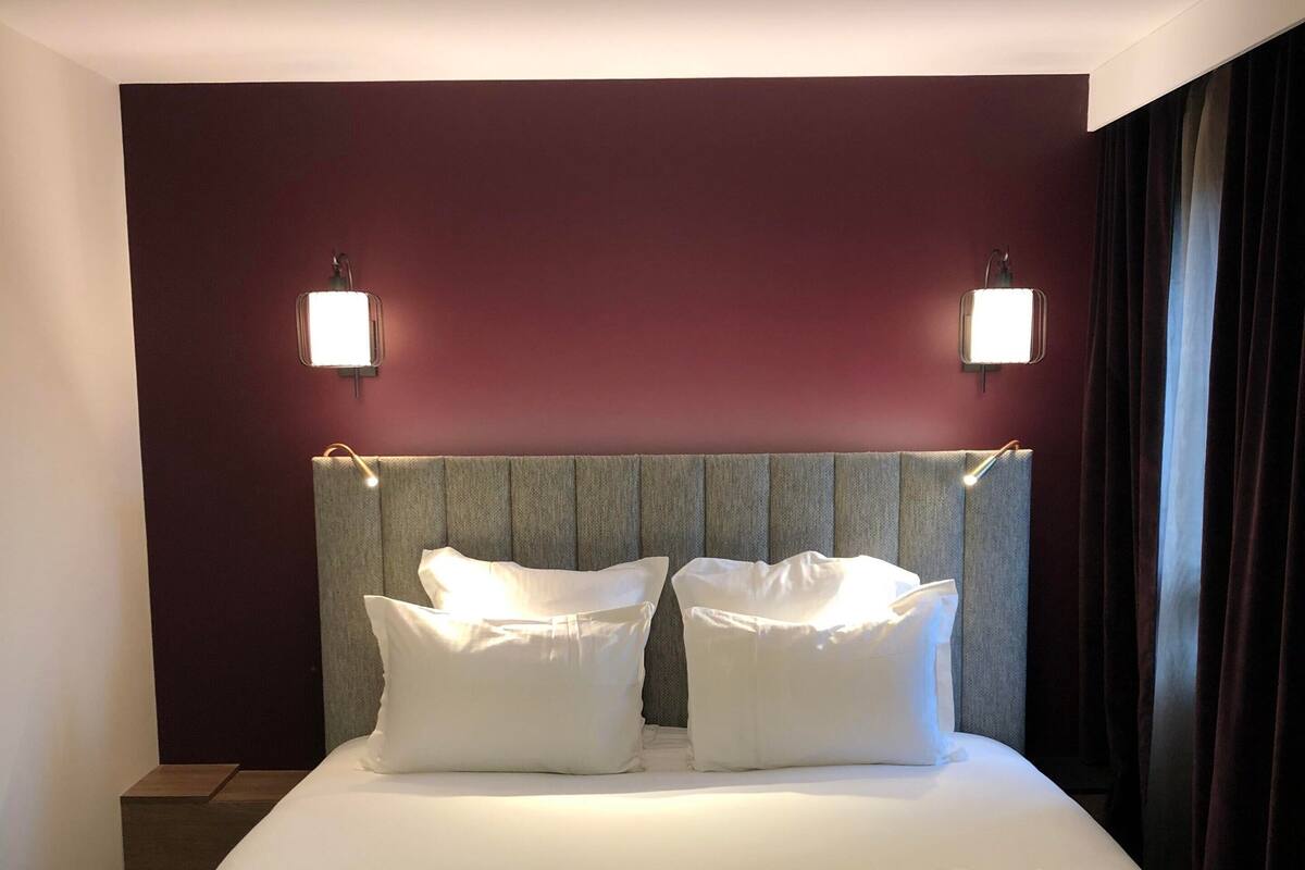 A neatly made bed with white linens and pillows, two bedside tables, and two wall-mounted lights.