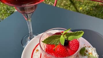 A dessert with strawberries, raspberries, and a yellow item on a white plate, and a glass of red drink with mint leaves on a table outdoors.
