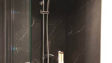 Una ducha moderna con cabezal de ducha tipo lluvia y cabezal de ducha de mano, sobre un fondo de pared de mármol oscuro.