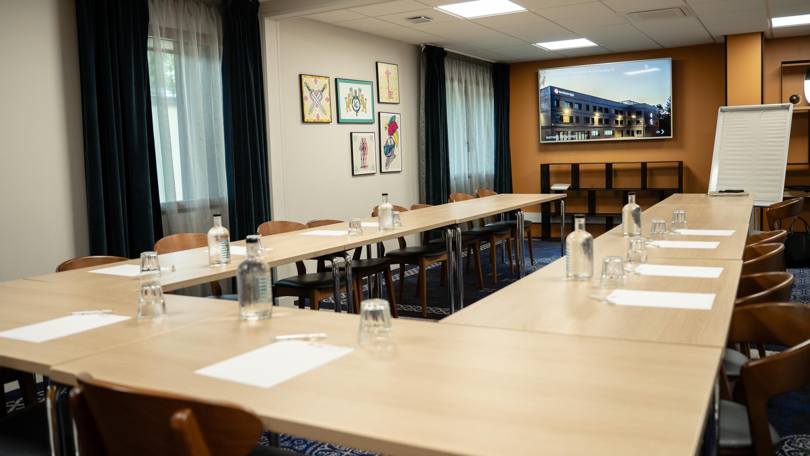 Un salón de conferencias con una larga mesa, sillas, botellas de agua y una pantalla de proyector que muestra una imagen de hotel.