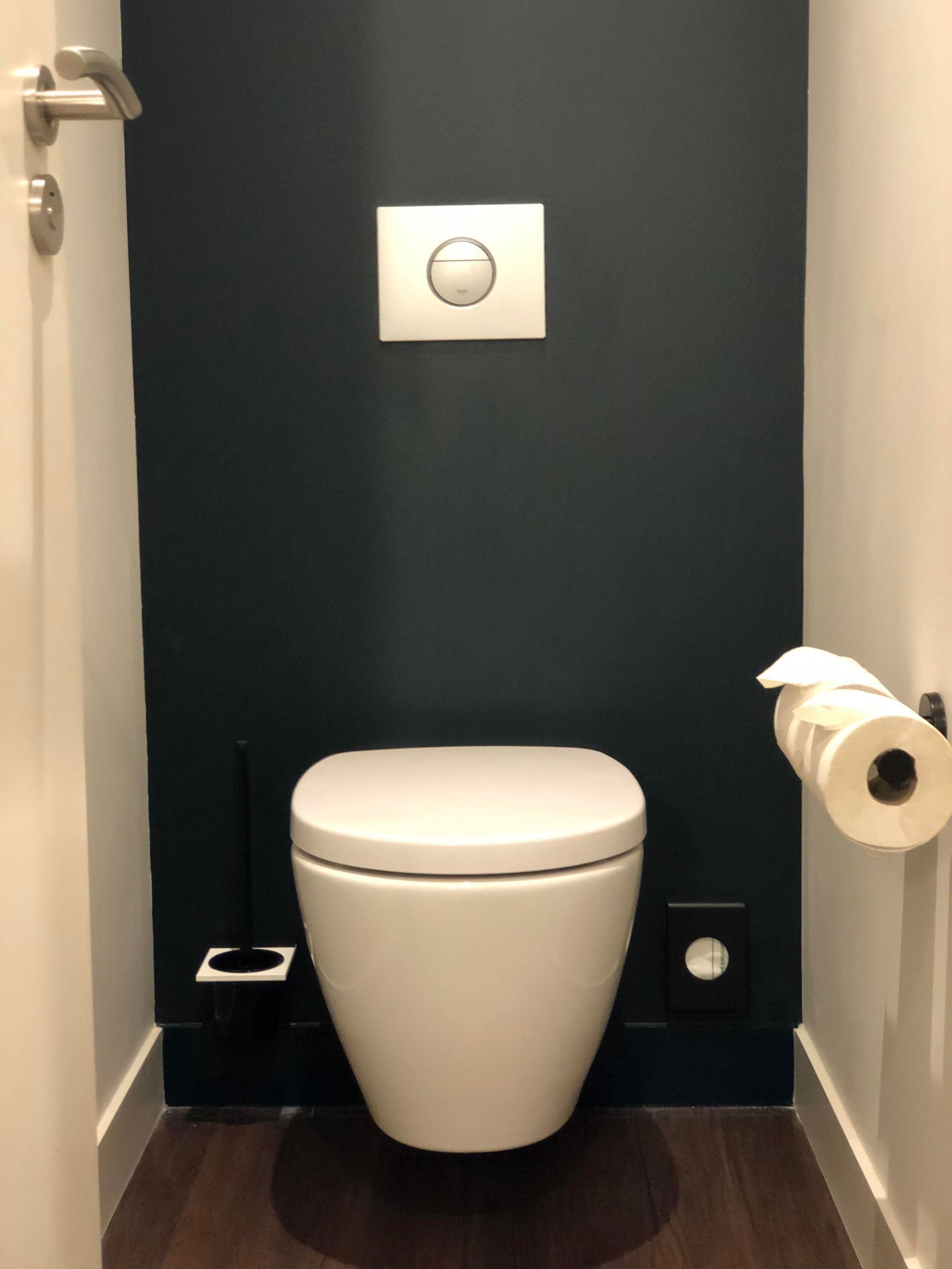 A modern bathroom with a white toilet, a dark wall, and a toilet paper holder.