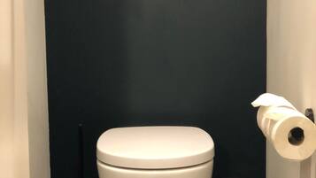 A modern bathroom with a white toilet, a dark wall, and a toilet paper holder.