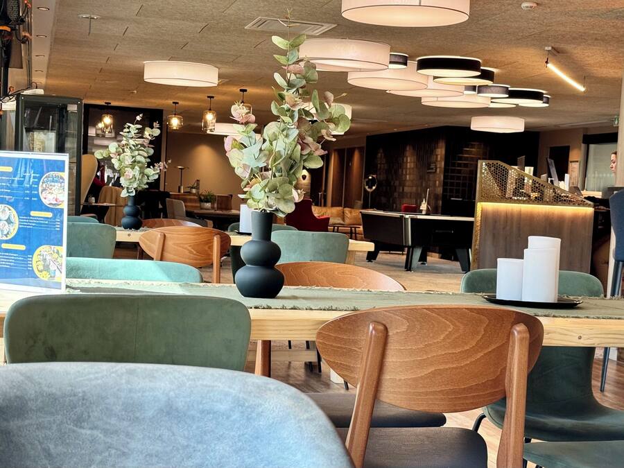 A modern interior with round tables, green upholstered chairs, and pendant lighting.