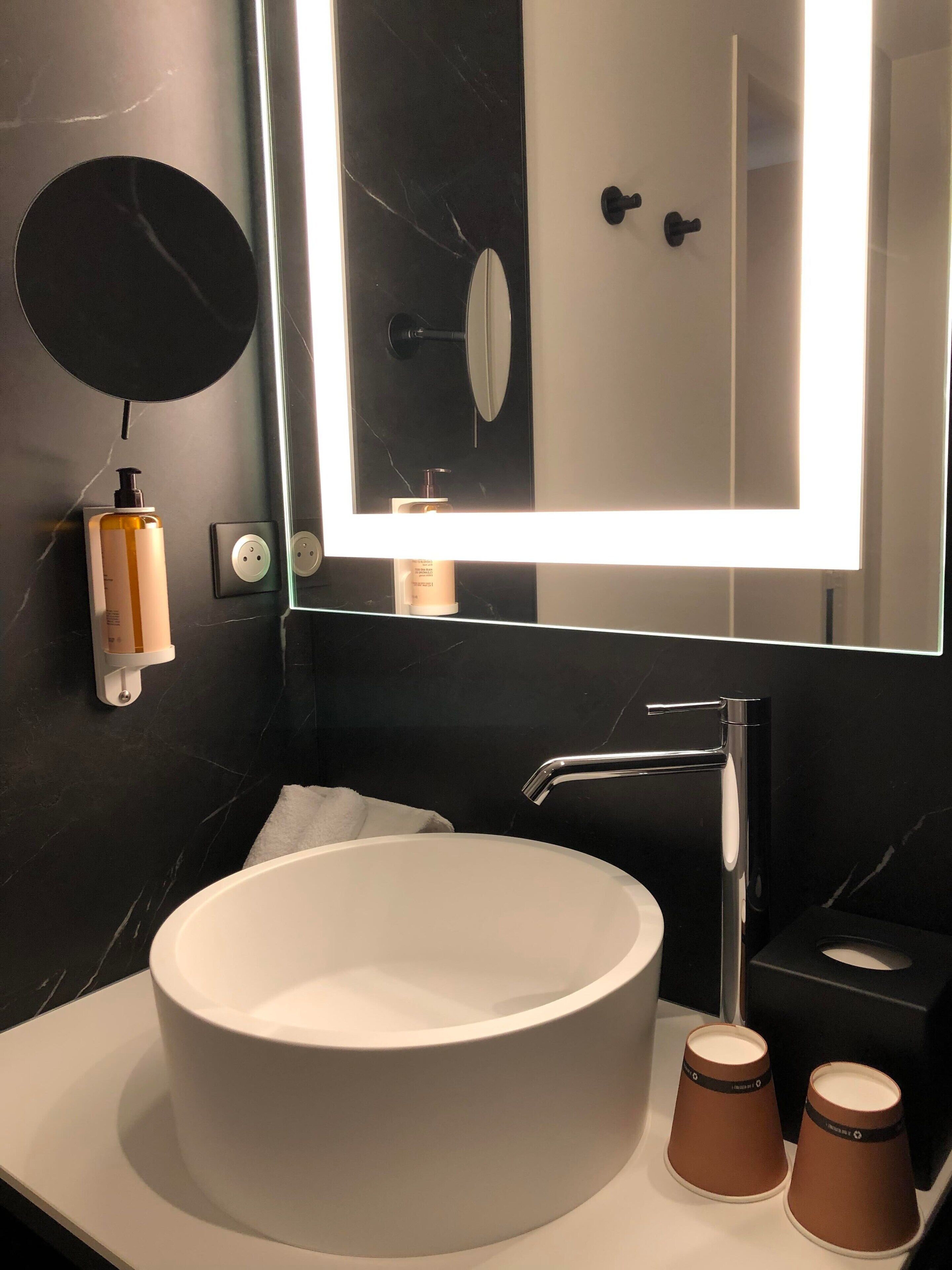 A modern bathroom with a large white sink, a mirror, and a black marble wall.