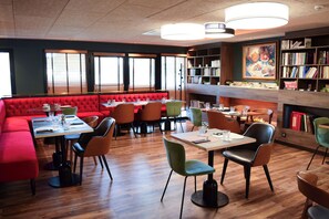 A modern restaurant with red seating, wooden tables, and a bookshelf. - Best Western Plus Le Conquerant Rouen Nord (Bois-Guillaume)