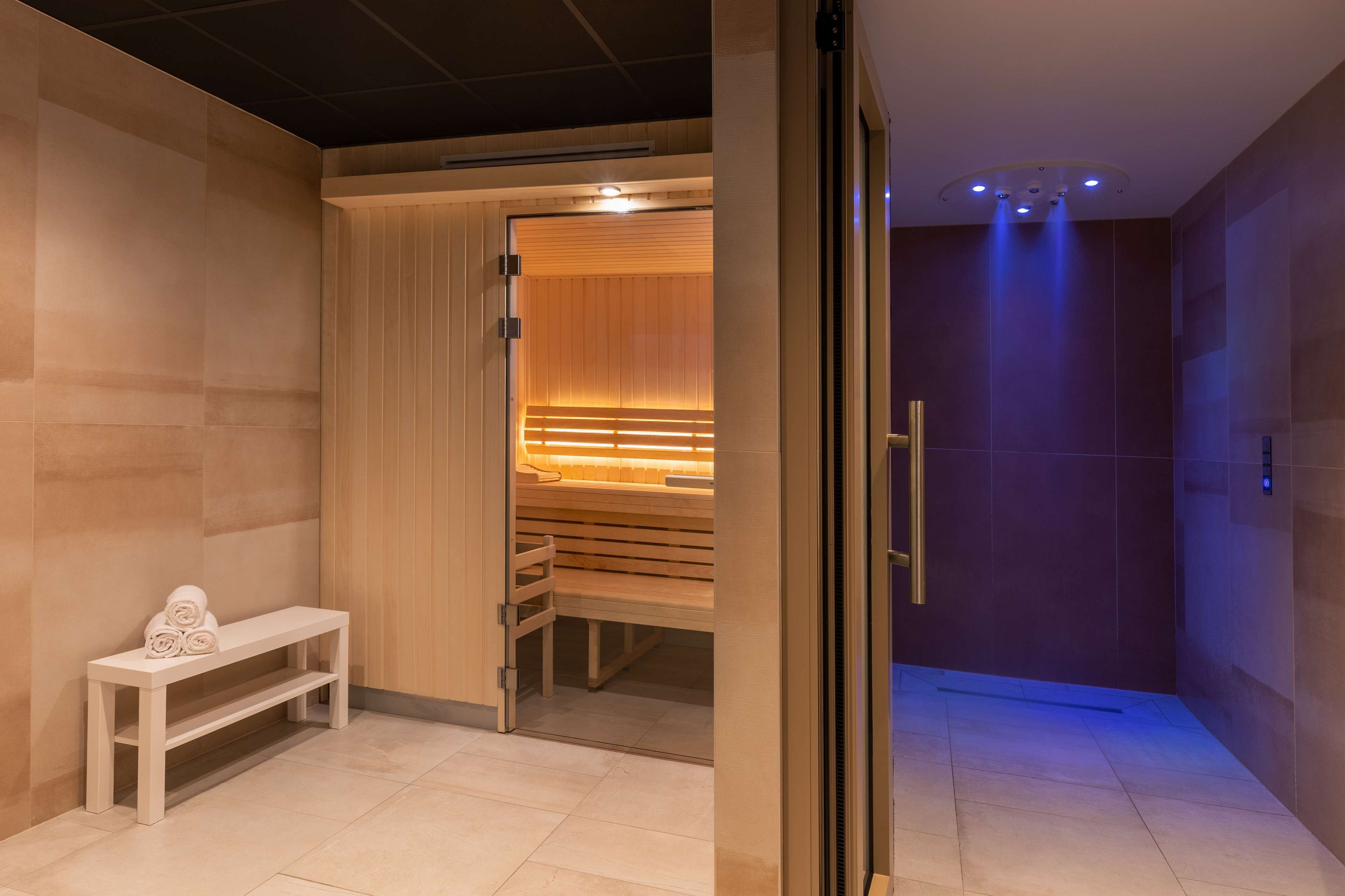 Un espacio moderno de spa con un banco de madera, una sauna y un ventanal que da a una habitación con bancos y toallas.