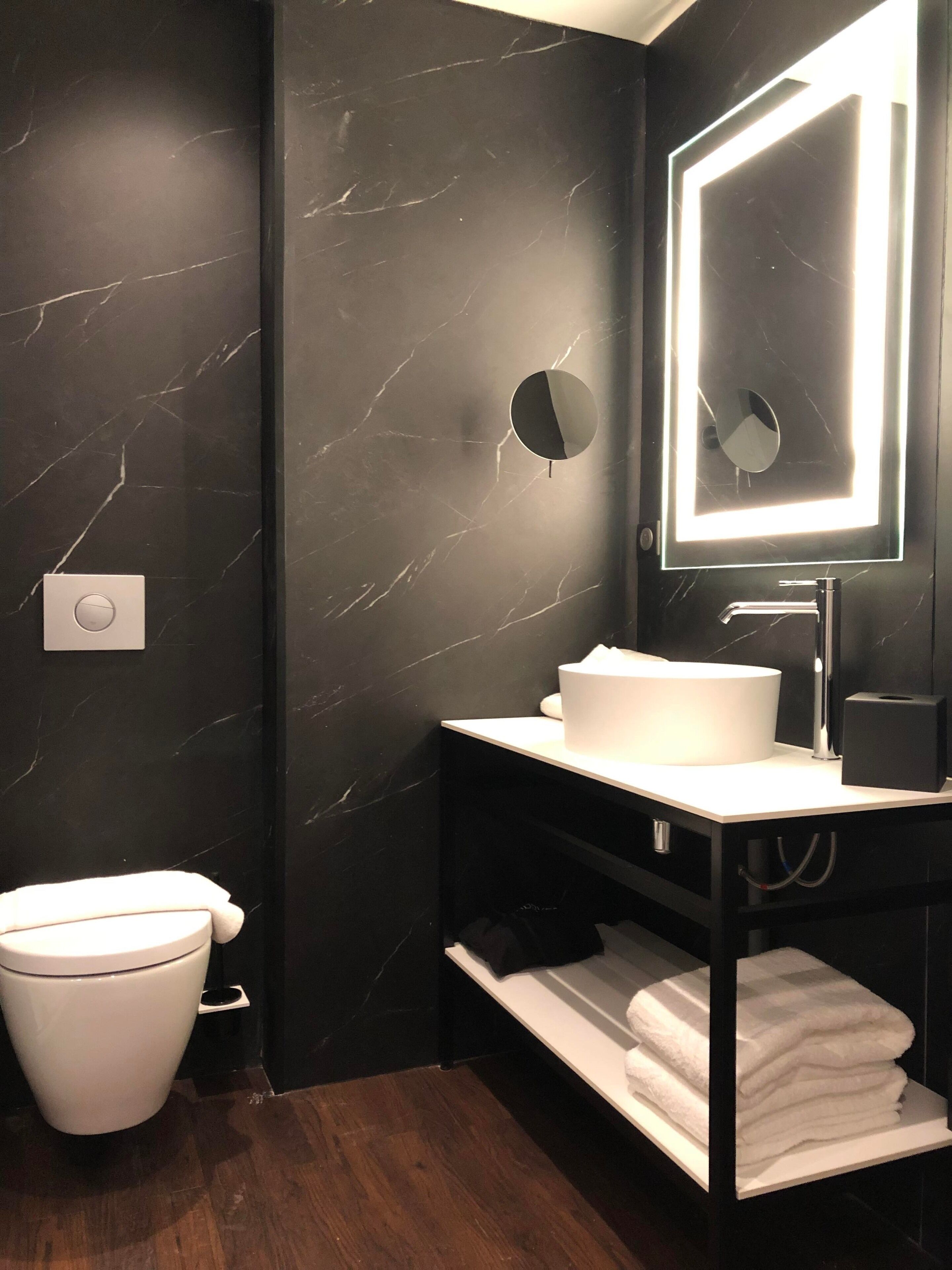 Un baño moderno con pared de mármol, inodoro, lavamanos con espejo y un perchero para toallas.