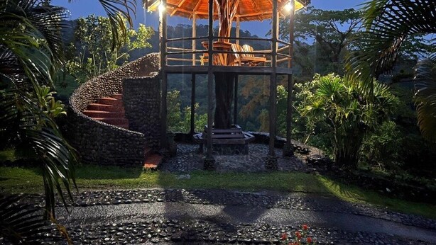 Un gazebo con una scala a chiocciola che conduce a una piattaforma in legno, immerso nel verde.