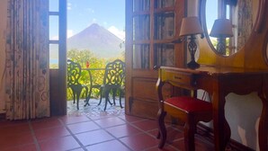 Una stanza con vista su una montagna, una scrivania in legno, una sedia e un balcone con sedie.