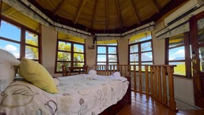 A room with a bed, wooden flooring, a balcony with a railing, and large windows. - Wide Luxury Home with Pool & Jacuzzi access & Amazing Volcano and Lake views (El Castillo)